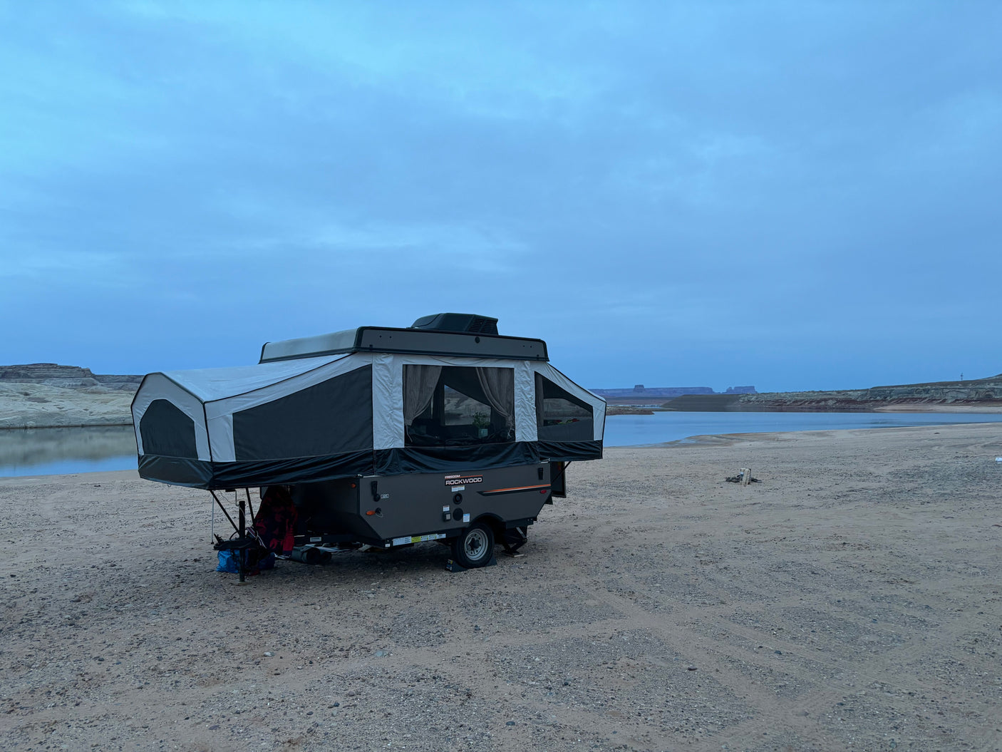 Pop-up rv rental set up for lakeside camping under a cloudy sky, offering a serene outdoor adventure by the water.