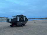 Pop-up rv rental set up for lakeside camping under a cloudy sky, offering a serene outdoor adventure by the water.