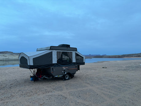 Pop-up rv rental set up for lakeside camping under a cloudy sky, offering a serene outdoor adventure by the water.