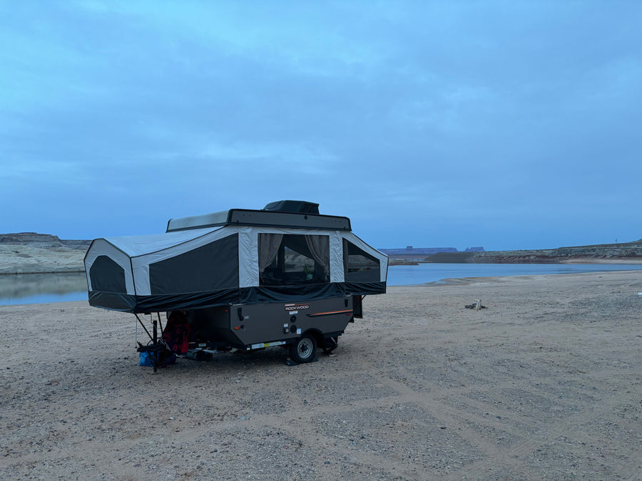 Pop-up rv rental set up for lakeside camping under a cloudy sky, offering a serene outdoor adventure by the water.
