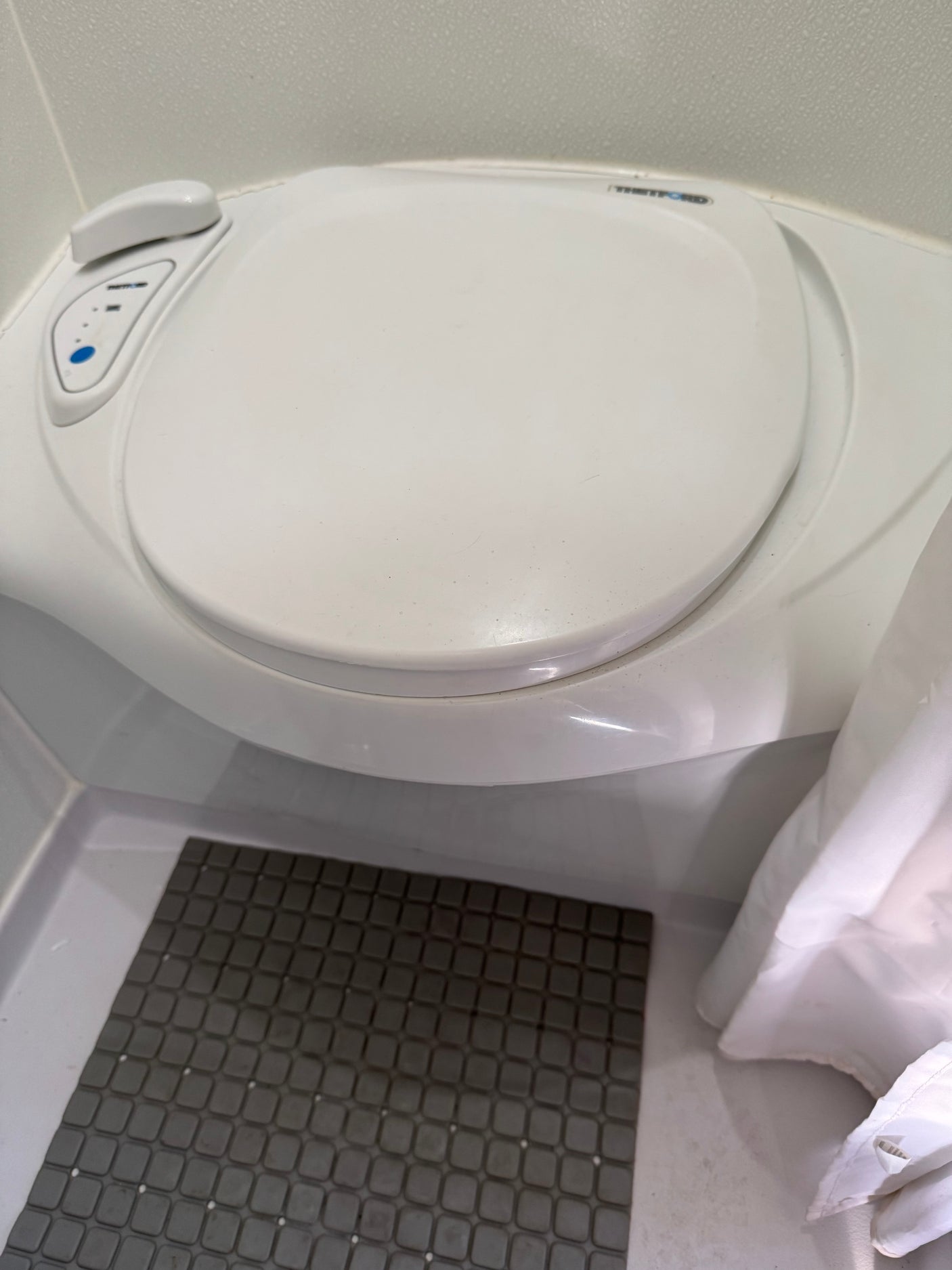 RV rental's compact Thetford toilet, with flush buttons, a grey mat, and a white shower curtain.