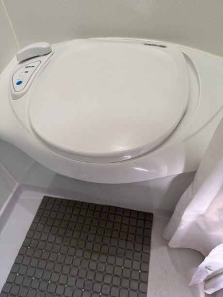 RV rental's compact Thetford toilet, with flush buttons, a grey mat, and a white shower curtain.