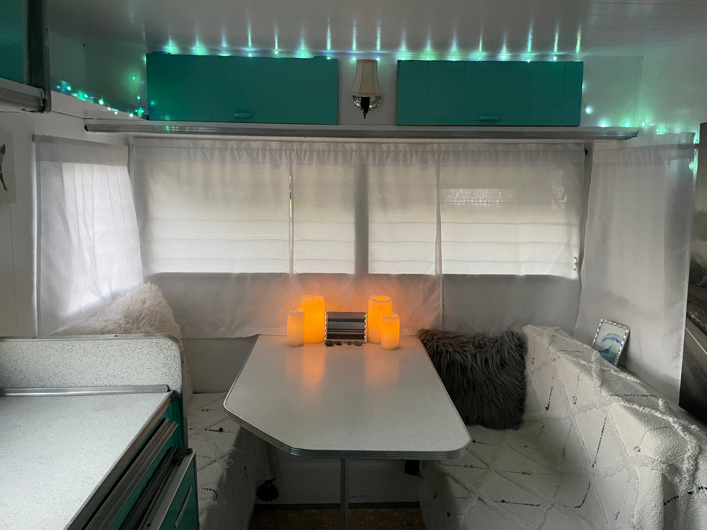 Inside a cozy RV rental: teal cabinets, green string lights, & soft LED candles illuminate the dinette. — photo 13