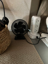 Compact setup in an RV rental: a small fan, power strip, and headphones in a woven basket, likely on a bedside table.
