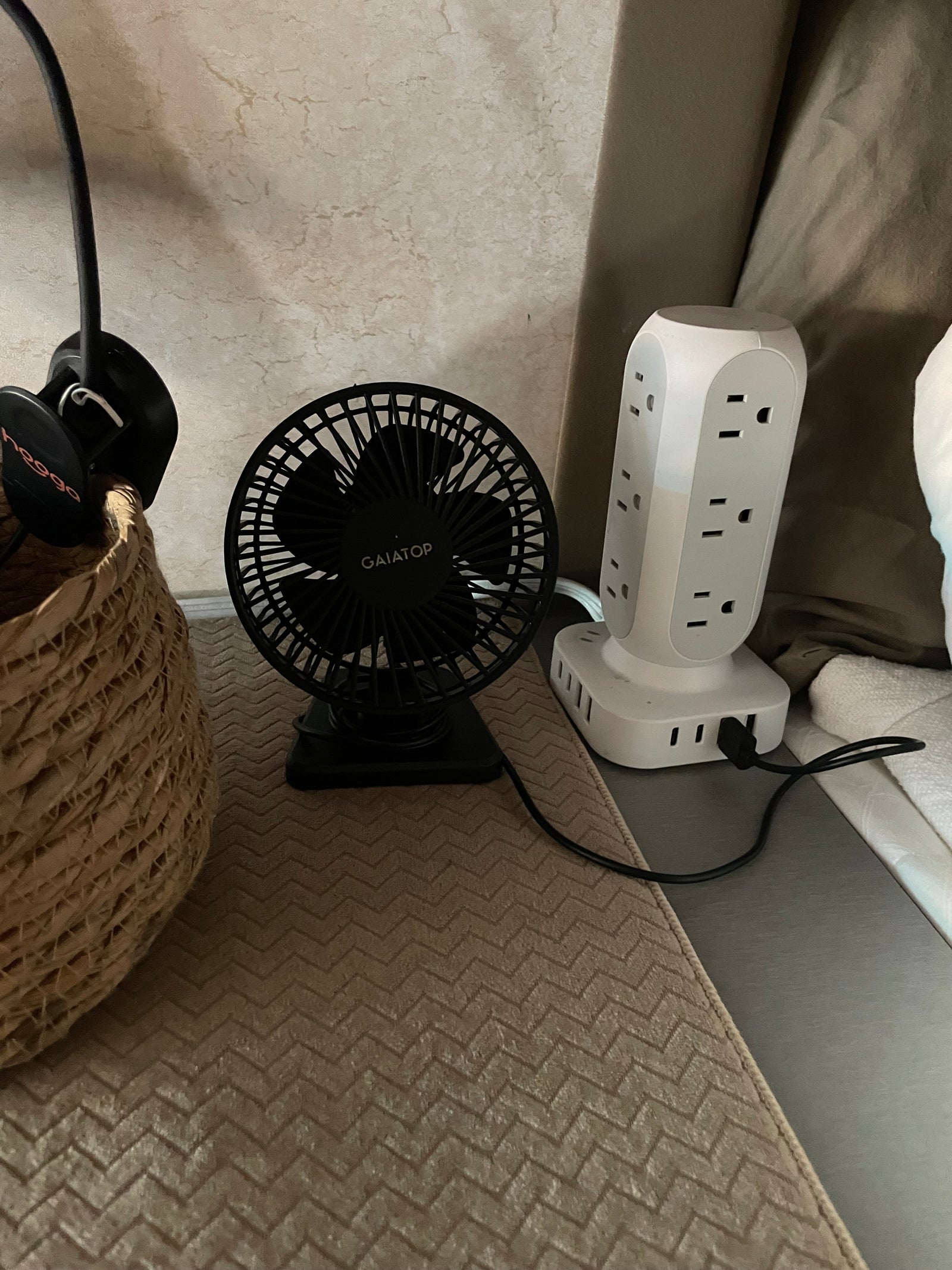 Compact setup in an RV rental: a small fan, power strip, and headphones in a woven basket, likely on a bedside table.