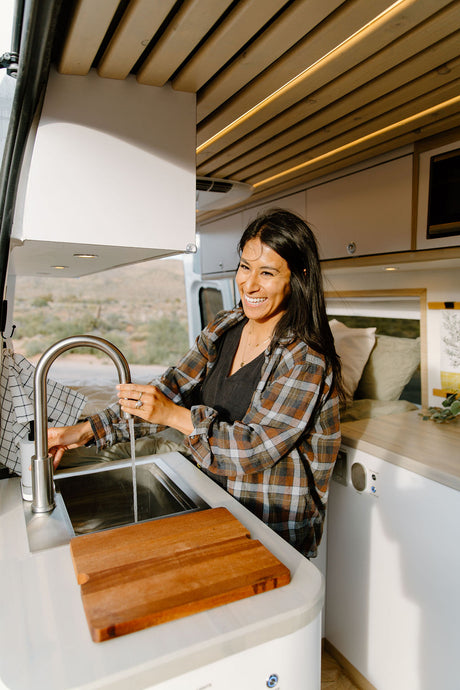 Smiling woman turning on the faucet in a spacious RV rental kitchen. Modern van interior is ideal for travel and adventures.