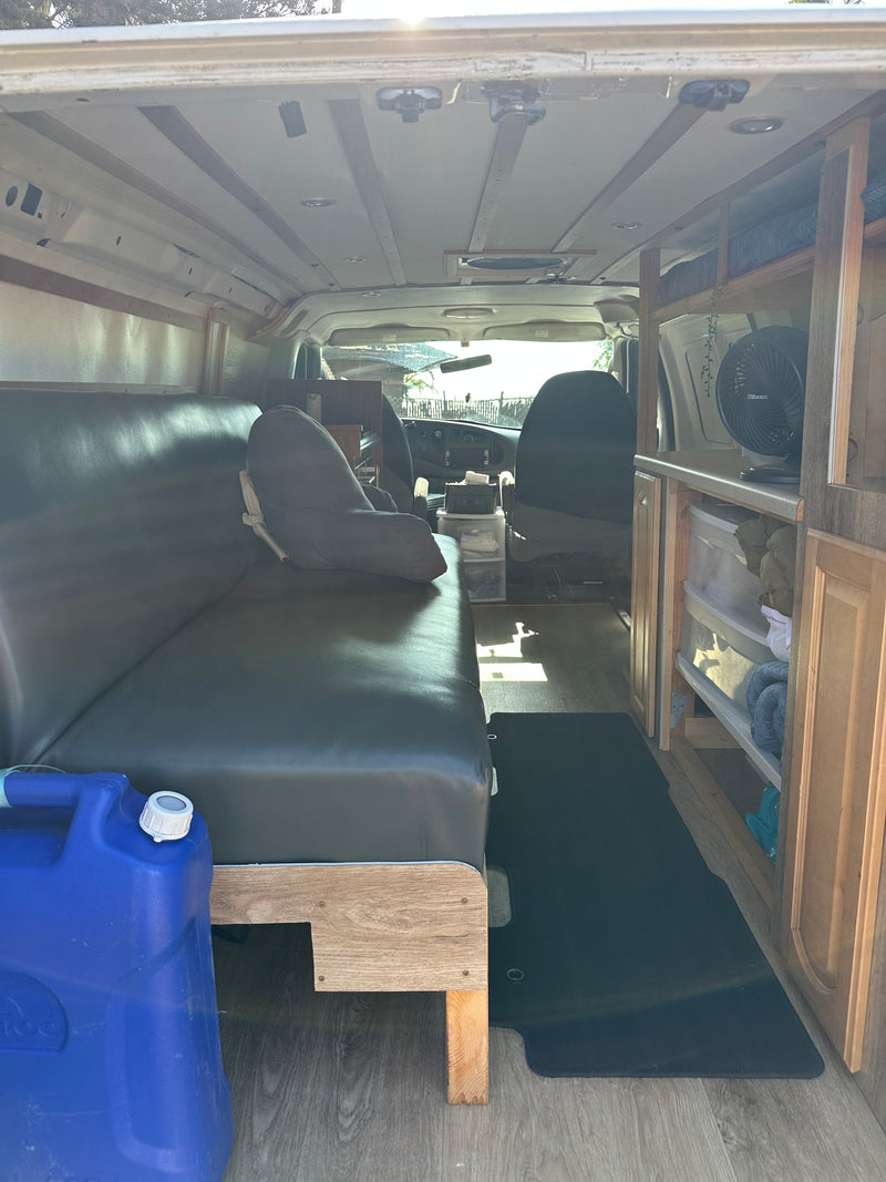 Interior of a converted camper van, perfect for an RV rental adventure. Shows a couch/bed, storage, and wooden flooring. — photo 18
