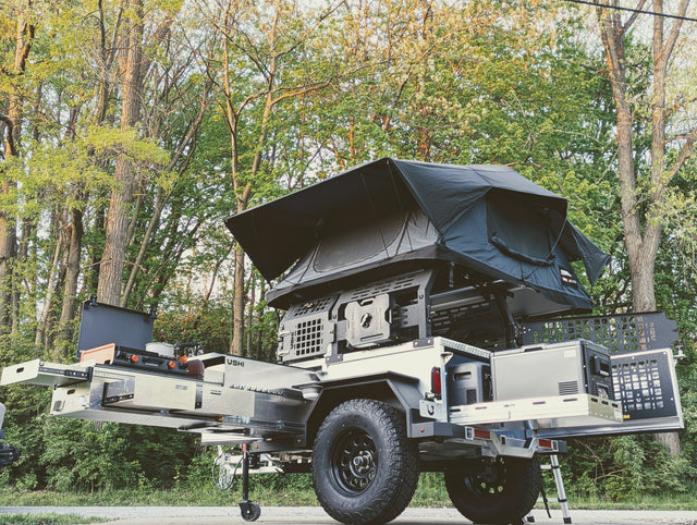 This off-road camping trailer, ideal for RV rental adventures, features a rooftop tent, pull-out kitchen, and fridge.