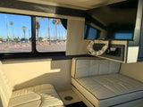 RV rental interior with cream-colored seating, a TV, and a scenic window view of a marina and palm trees.