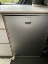 Sleek Isotherm stainless steel refrigerator in an RV rental setup, featuring a wood-layered counter and integrated handle.