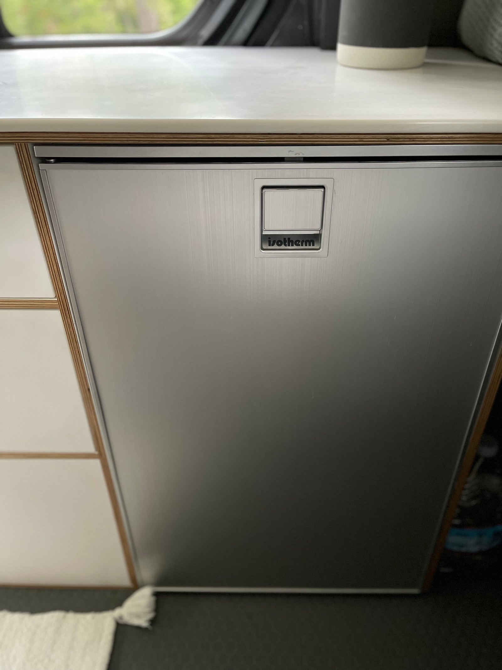 Sleek Isotherm stainless steel refrigerator in an RV rental setup, featuring a wood-layered counter and integrated handle.