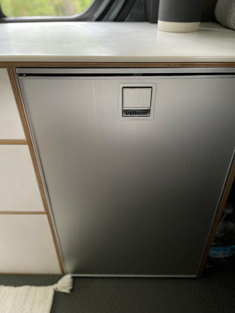 Sleek Isotherm stainless steel refrigerator in an RV rental setup, featuring a wood-layered counter and integrated handle.