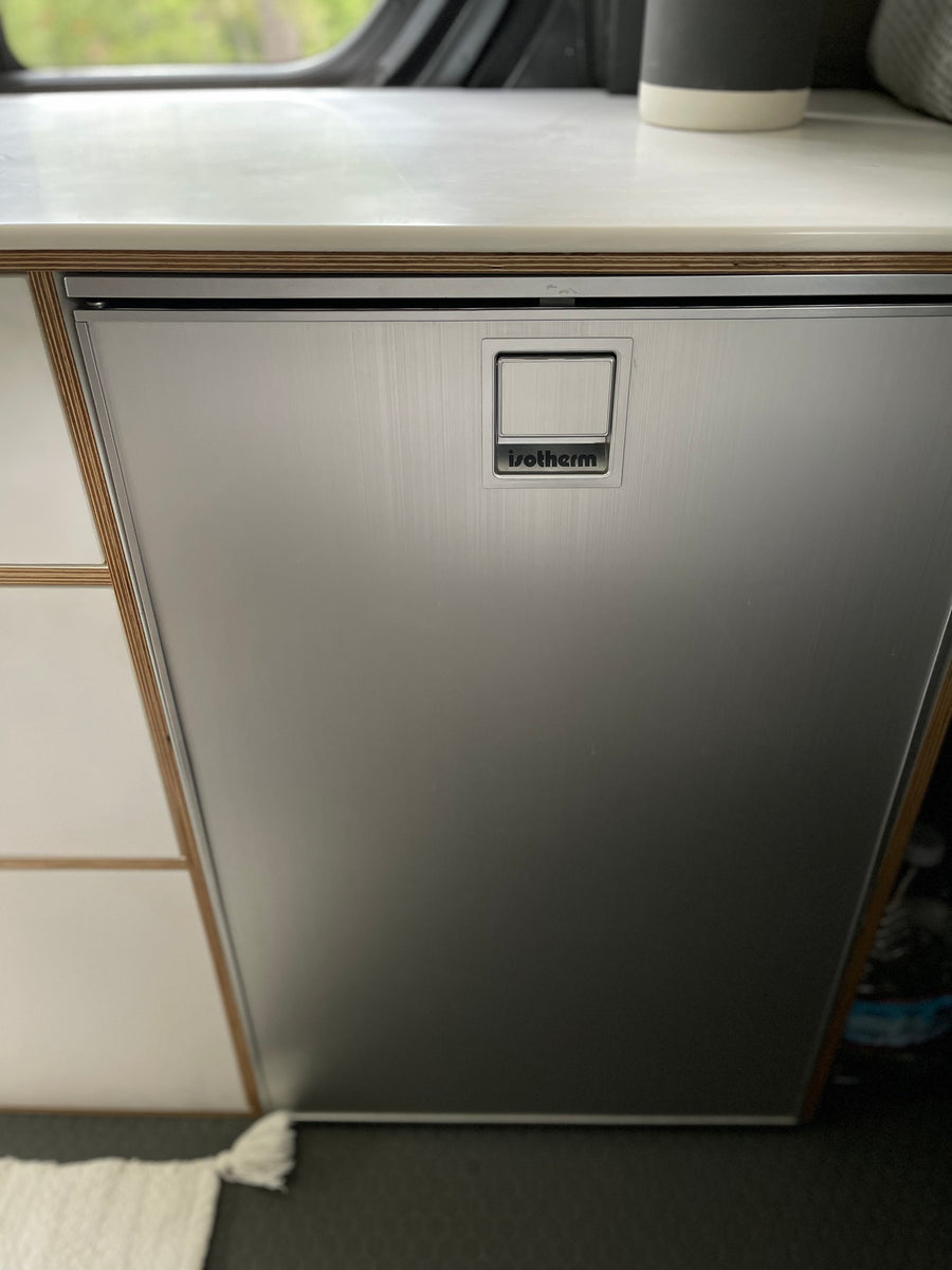 Sleek Isotherm stainless steel refrigerator in an RV rental setup, featuring a wood-layered counter and integrated handle.