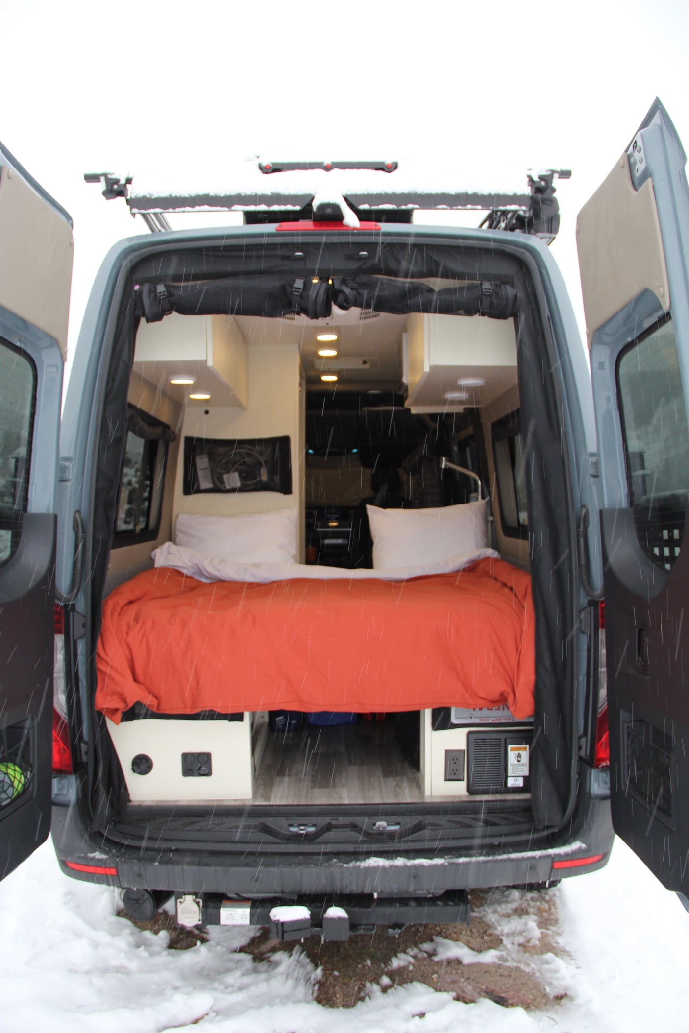 Explore in comfort with this RV rental camper van. Rear doors open show a cozy bed, custom interior, ready for winter travel.