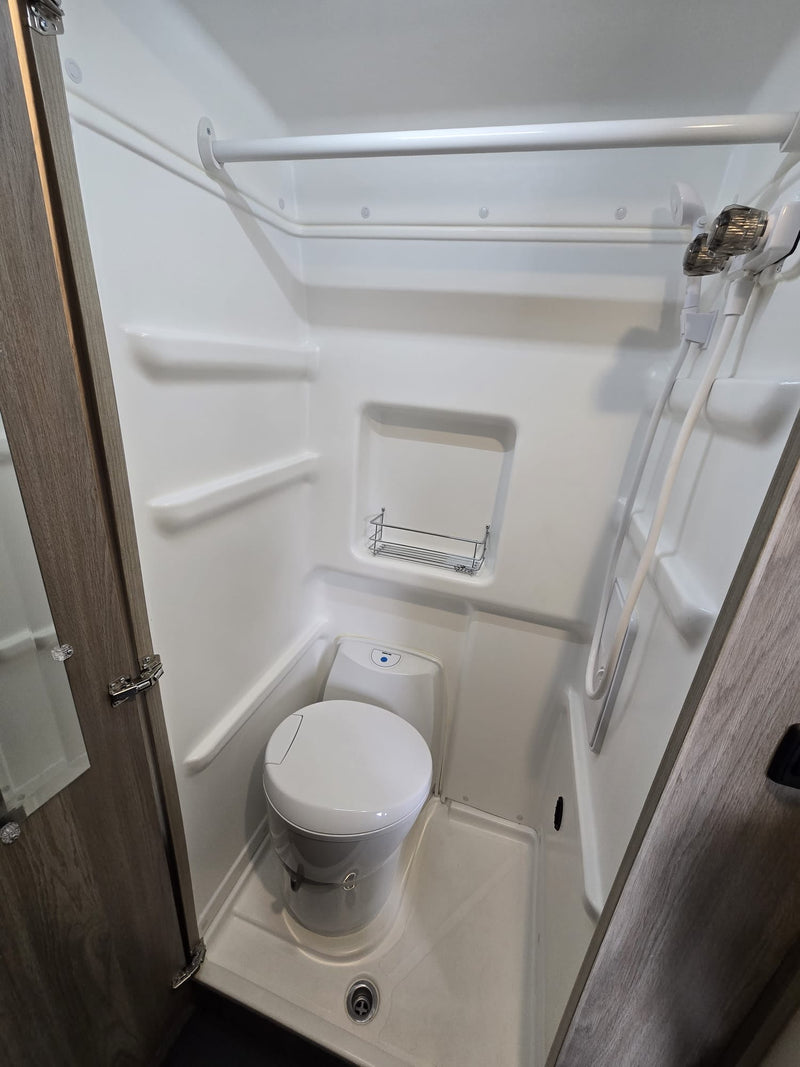 Interior of an RV rental bathroom, featuring a compact toilet, shower, and built-in shelves. — photo 7