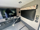 Modern rv rental interior with mounted TV, stereo, window blind, and controls for a comfortable travel experience.