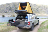 RV rental: Ford truck camper with pop-up tent & pull-out kitchen by river. Ideal overlanding setup for remote camping.
