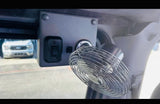 RV rental interior: a small metal fan, control panel with switches, and outlet for comfort. A truck is visible outside.