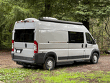A silver camper van, ideal for RV rental, is parked outdoors. Features include a roof AC unit and awning, surrounded by green trees.