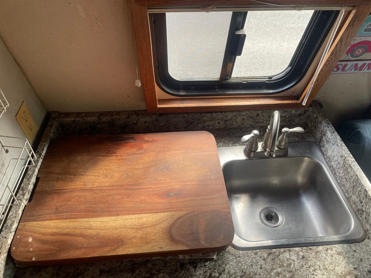 Compact RV rental kitchen counter featuring a sink, faucet, and large wooden cutting board, ideal for preparing meals on the road. — photo 3
