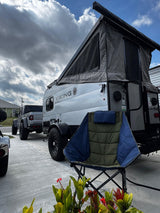 A grey Jeep Gladiator tows a Viking pop-up RV rental, ready for an outdoor camping adventure. A green chair sits nearby.