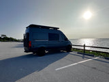 This Storyteller Overland camper van by the water, ideal for an rv rental adventure. Sun glints on the waves.