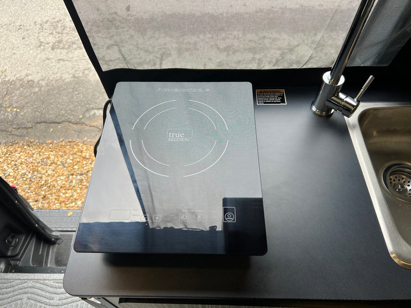 RV rental kitchenette with a sleek True Induction cooktop and sink. Includes safety warning about a nearby curtain. — photo 16