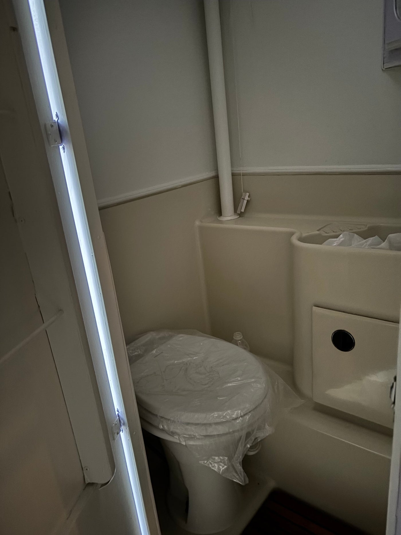 Compact RV rental bathroom with a new toilet (covered in plastic), integrated sink/shower, and bright vertical lighting. — photo 5