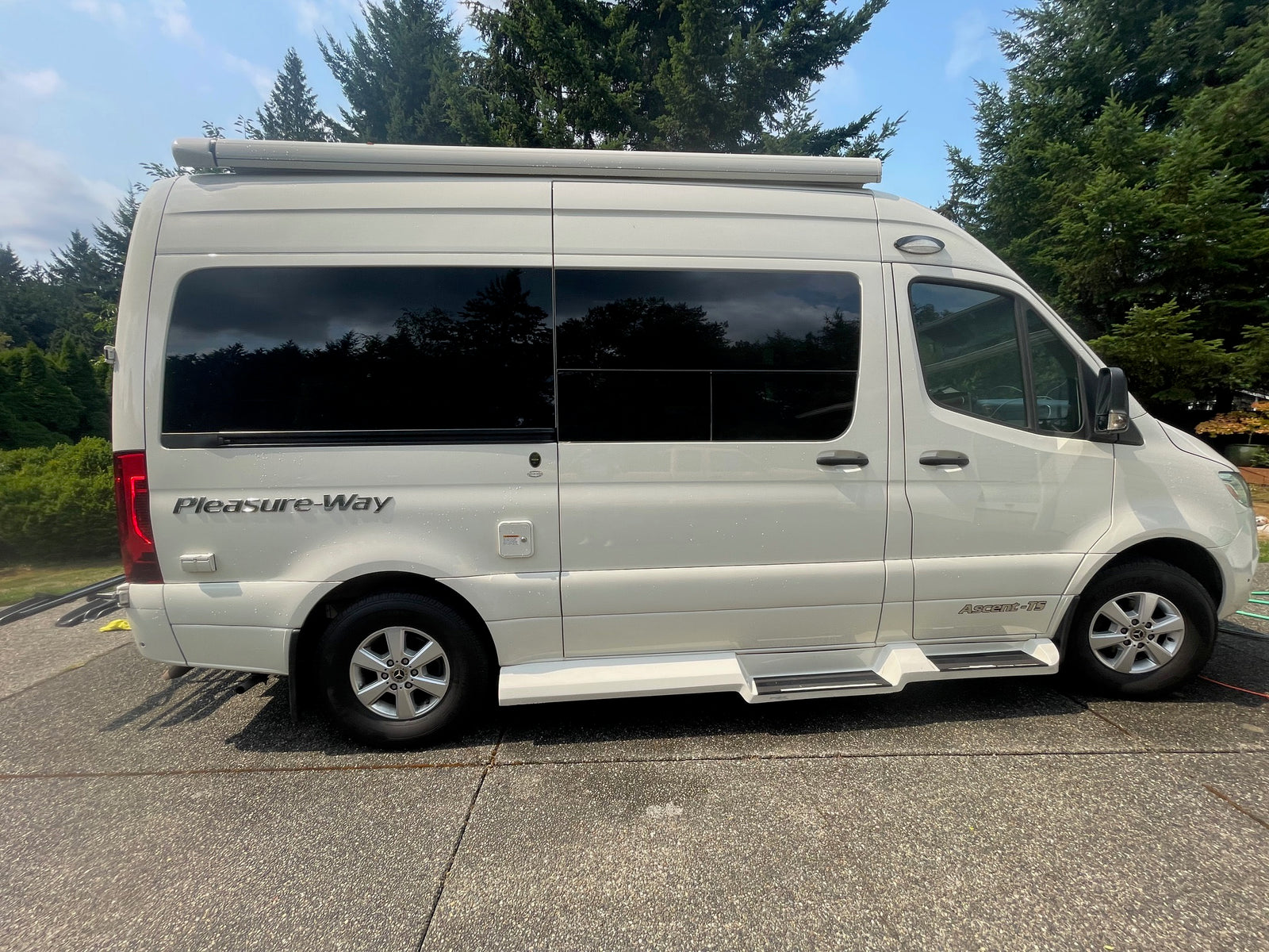 Side view of a white Pleasure-Way Ascent-TS RV rental with tinted windows, parked on a sunny day.