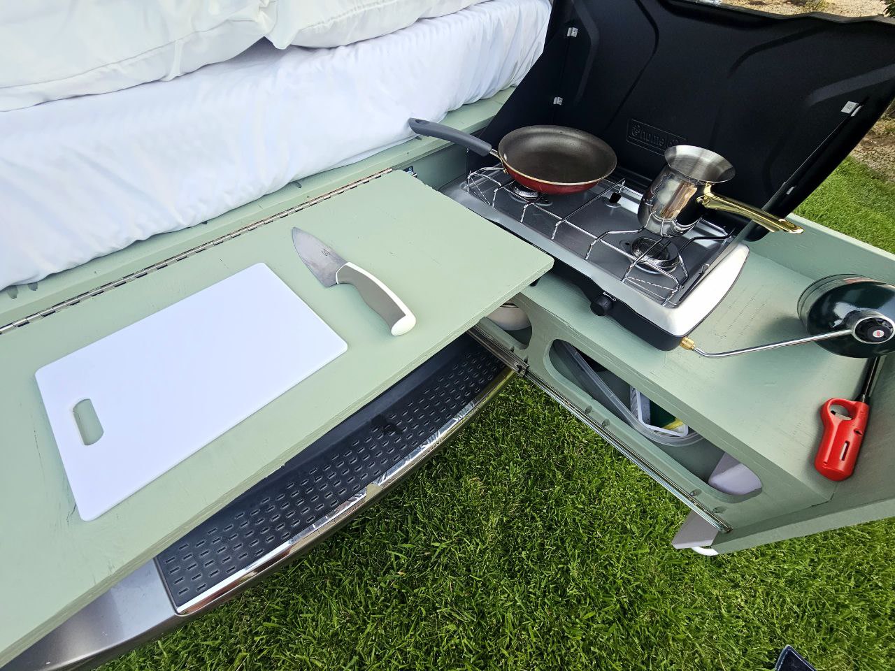 RV rental outdoor kitchen setup. Features pull-out counter with cutting board, stove with pan/pot, and propane lantern. Perfect for camping! — photo 15