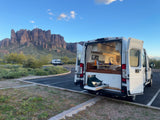 Experience van life! This RV rental features an open campervan with an outdoor kitchen, parked against stunning desert mountains.