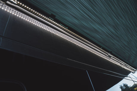 Bright LED strip lights line the side of an RV rental, providing illumination under its awning for enhanced outdoor experiences.