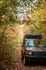 Black Land Rover with rooftop tent on a vibrant autumn trail. Perfect for overlanding and nature exploration. Consider an RV rental for your next outdoor adventure!