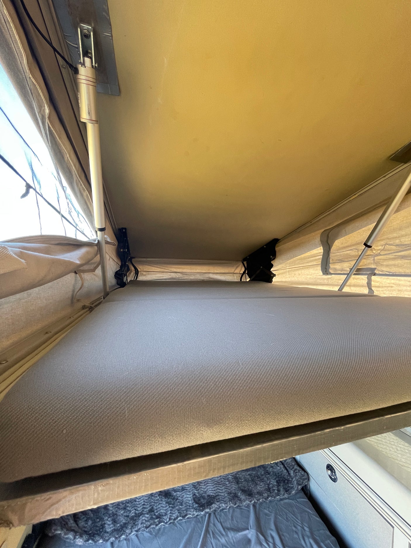 Cozy RV rental pop-up bed interior with canvas walls & support poles, showing a comfortable camping sleep space.