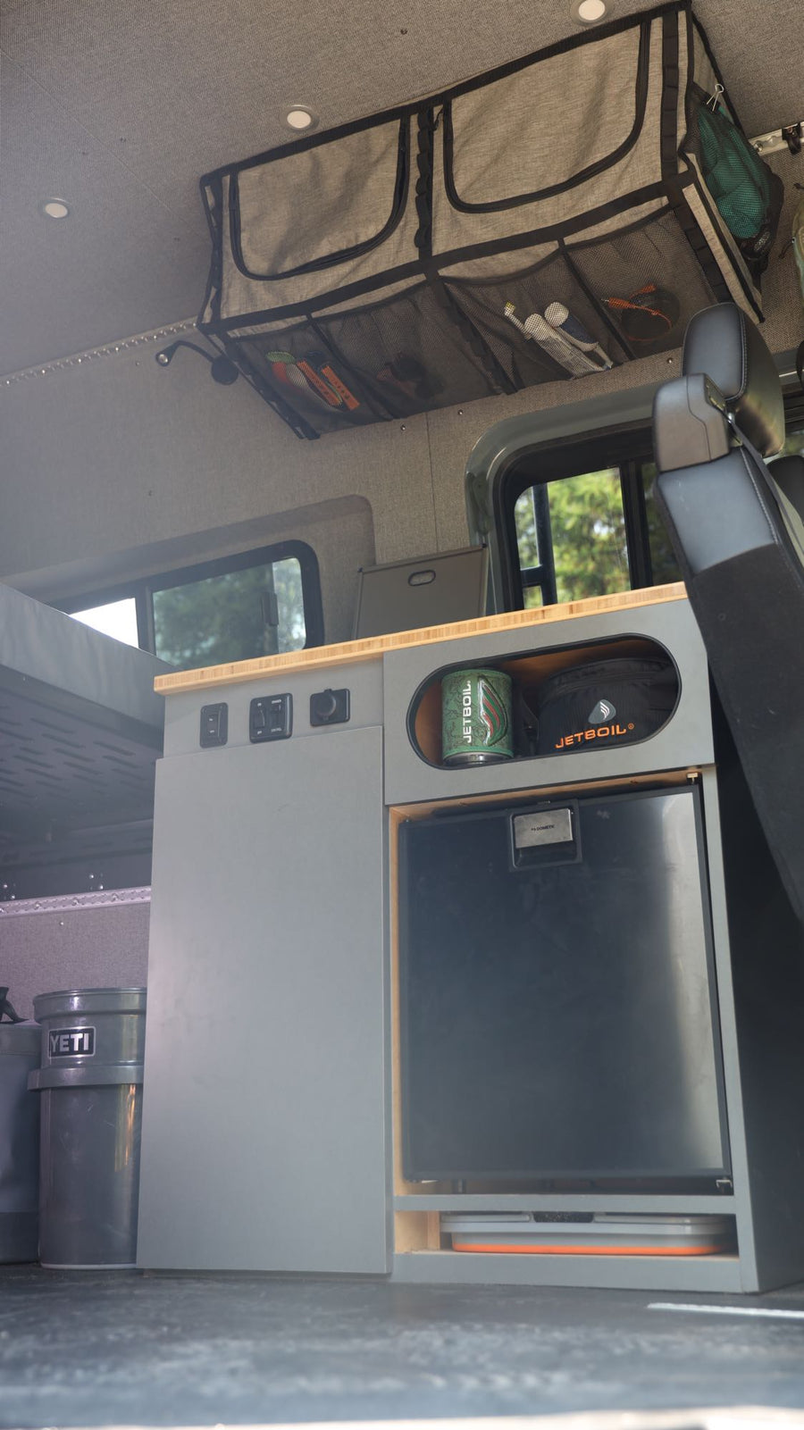 View inside an RV rental showing organized overhead storage, a built-in fridge, and countertop amenities.