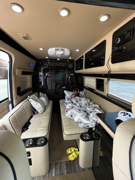 Plush RV rental interior: A person relaxes on a cozy bed inside a luxury van, perfect for comfortable travel.