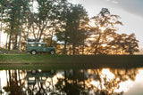 Green Land Rover with rooftop tent beside a lake at sunset. Your ideal **RV rental** for scenic outdoor adventures.