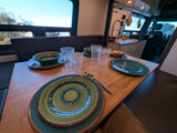 Inside a comfortable **RV rental**: A dining table set with colorful dishes and glasses, a functional kitchen, and scenic outdoor views.
