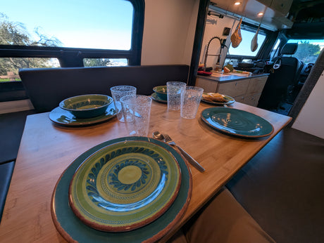 Inside a comfortable **RV rental**: A dining table set with colorful dishes and glasses, a functional kitchen, and scenic outdoor views.