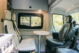 Inside a modern rv rental: bright camper van interior with passenger seating, a small table, and a scenic window view.