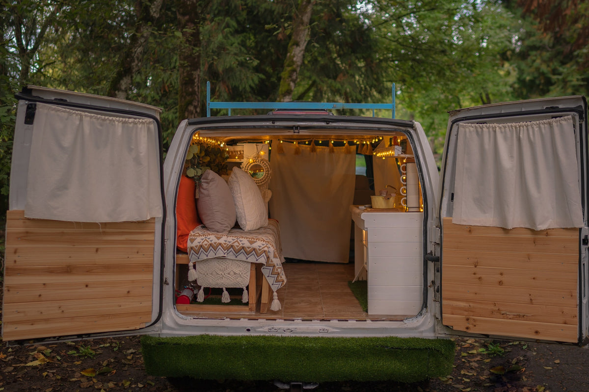Step into this cozy RV rental van! Rear doors open to reveal a custom, lit interior with bed & kitchen setup.