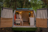Step into this cozy RV rental van! Rear doors open to reveal a custom, lit interior with bed & kitchen setup.