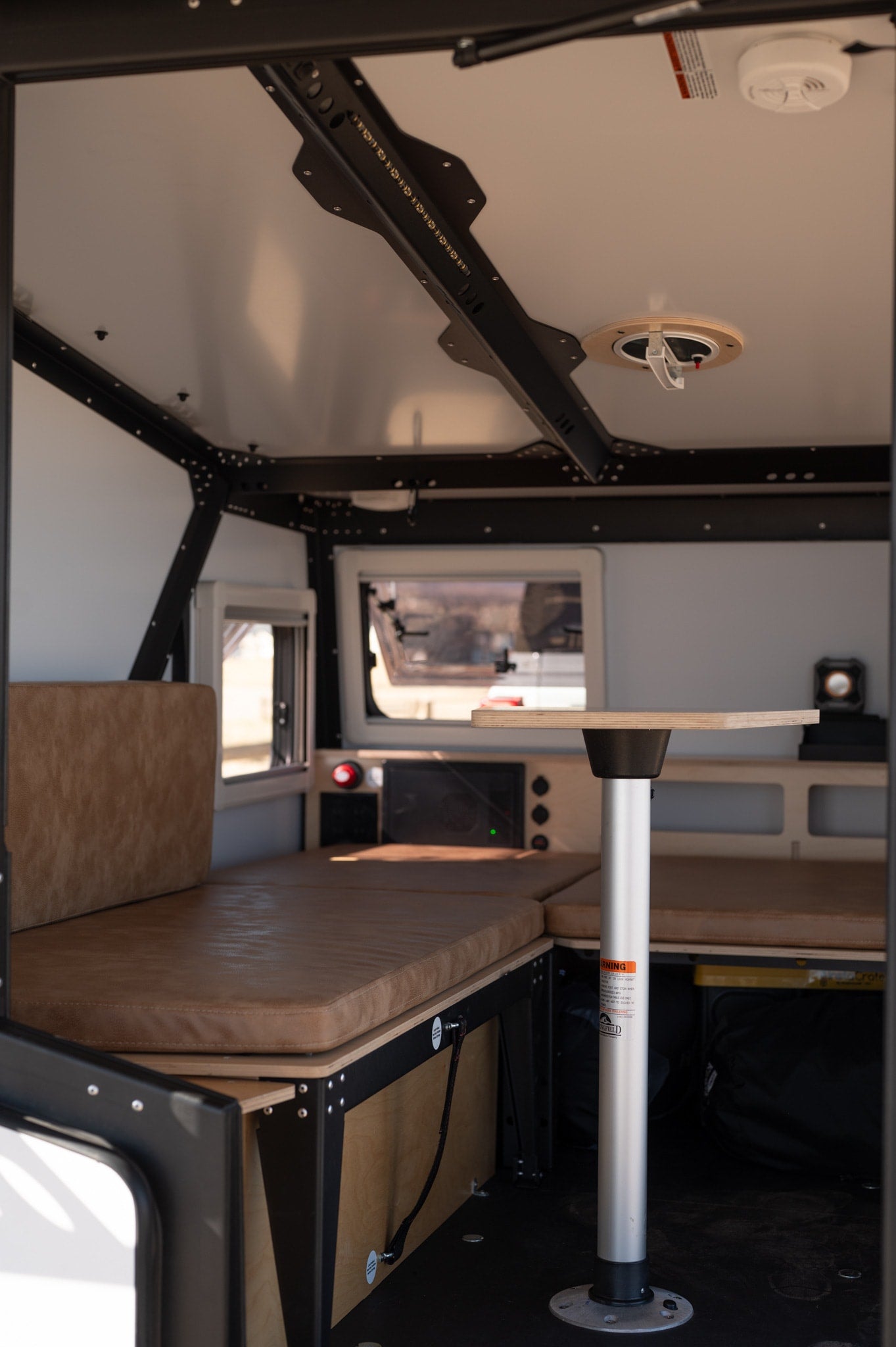 Step into your next rv rental adventure! This camper interior offers cozy brown cushioned seating, a functional table, and bright windows.