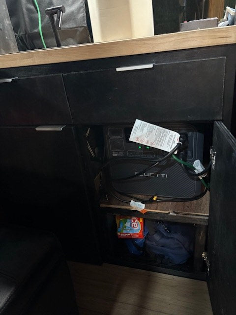  wood-paneled garage.|Bluetti portable power station & water tank in an RV rental's under-counter storage area.|Inside this RV rental: Alpicool portable freezer — photo 2