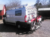 White Ram ProMaster camper van, with a rooftop rack and rear motorcycle carrier. Ideal for RV rental adventures.