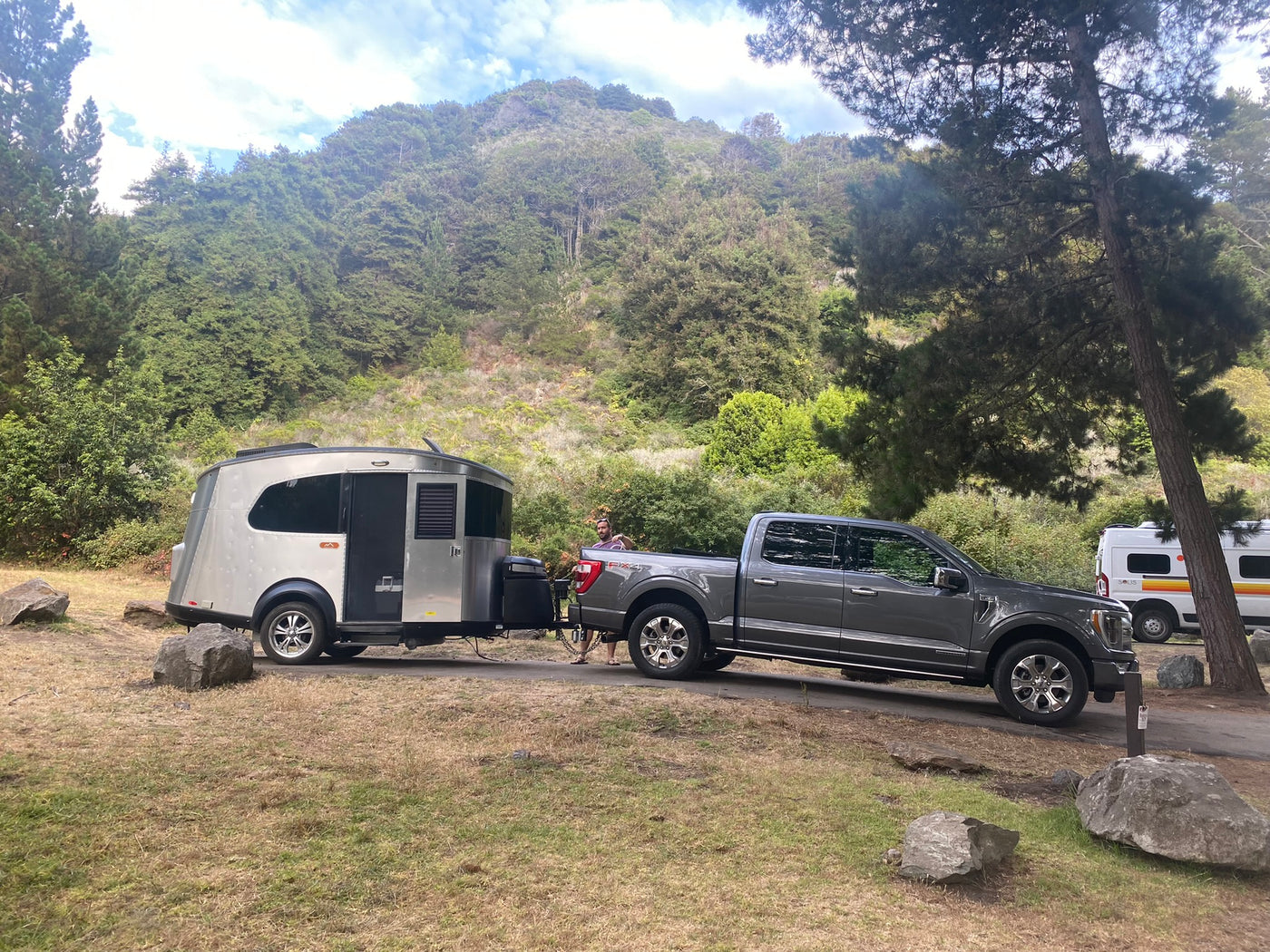 RV rental adventure! A grey pickup truck tows a silver travel trailer at a lush, forested campsite, with another camper van nearby. — photo 8