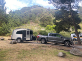 RV rental adventure! A grey pickup truck tows a silver travel trailer at a lush, forested campsite, with another camper van nearby.