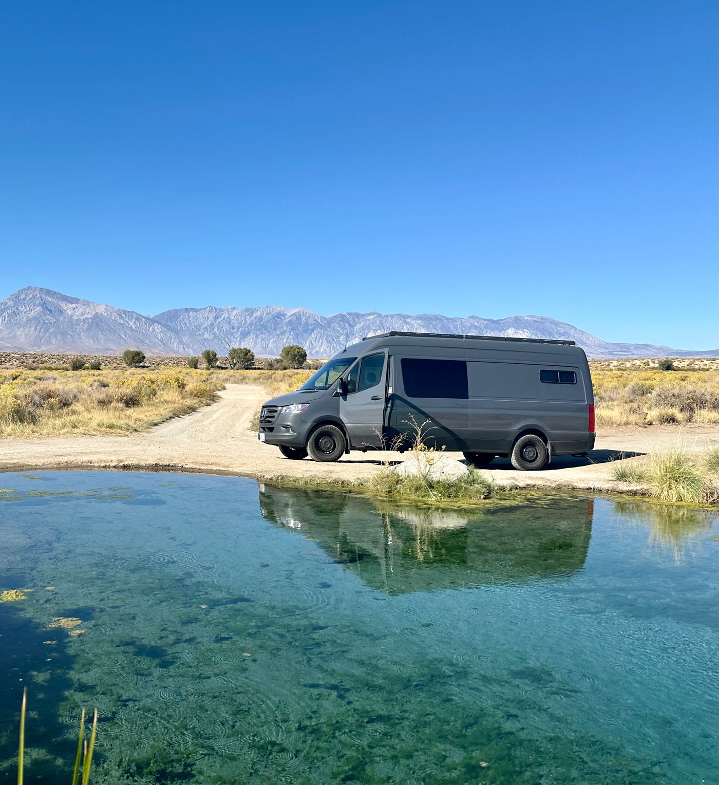 Grey RV rental (Sprinter van) by a clear, turquoise natural spring with mountains. Perfect for scenic nature trips. — photo 2