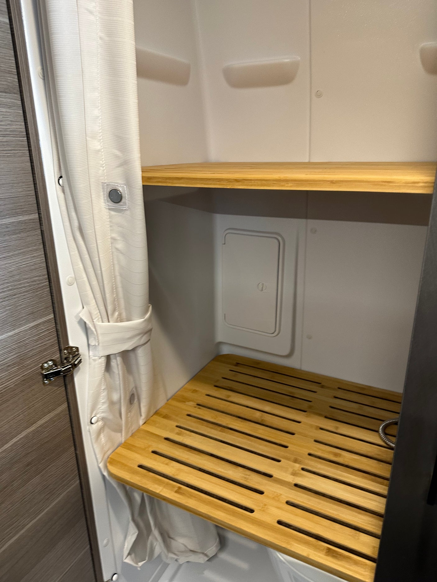 RV rental shower: compact design with white curtain, magnetic closures, bamboo shelves, and a slatted floor mat for utility.