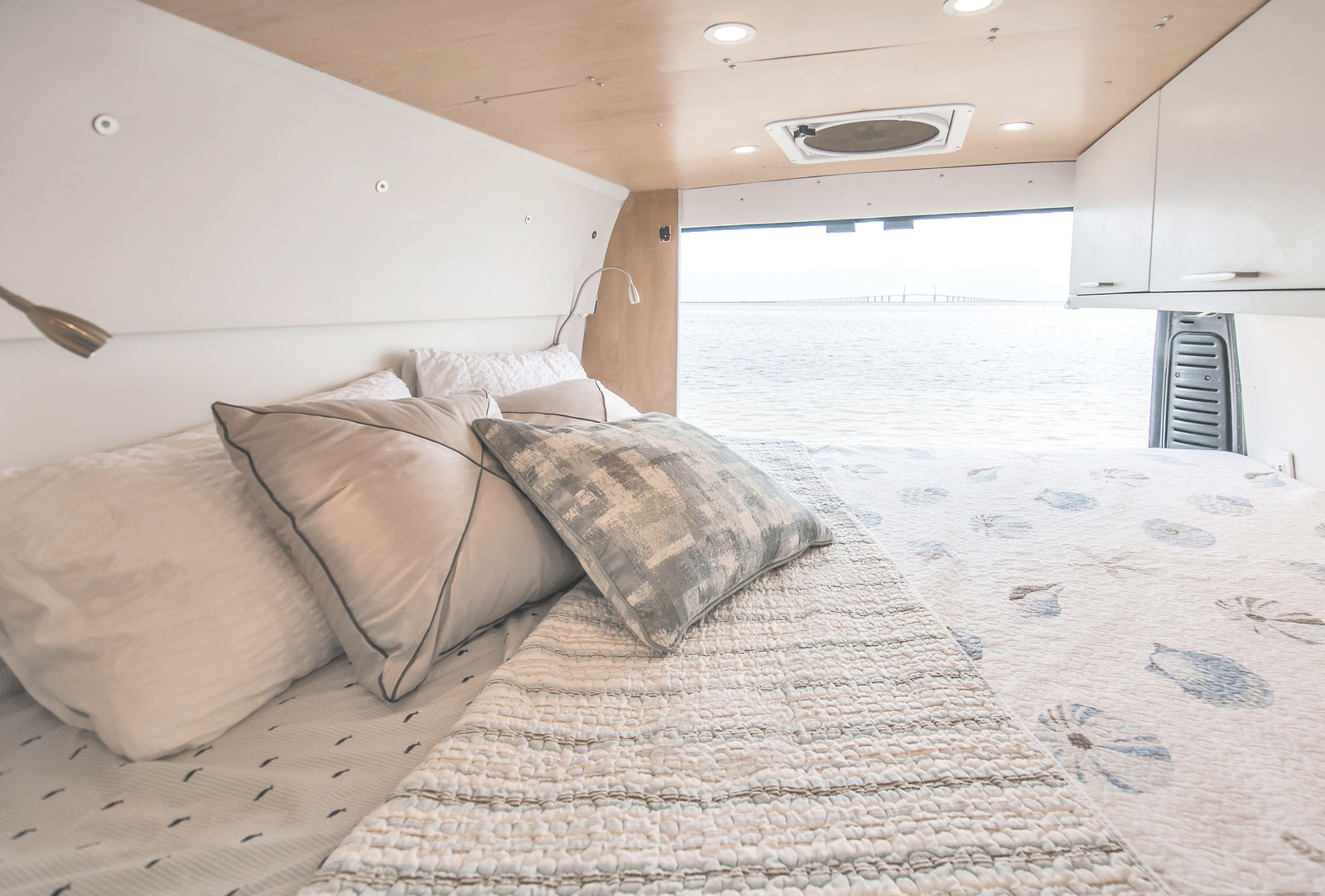 RV rental: Interior of a bright van bedroom with a comfortable bed and panoramic water view, including a bridge.